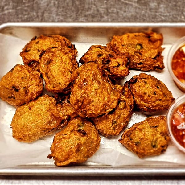 A tray of golden-brown Thai fish cakes with two small containers of dipping sauce.