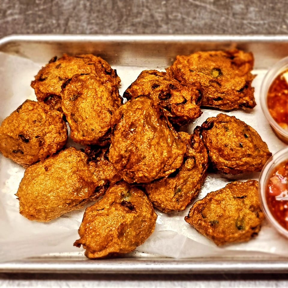 A tray of golden-brown Thai fish cakes with two small containers of dipping sauce.