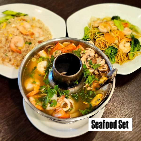 A Thai seafood hot pot, shrimp fried rice, and shrimp noodles with broccoli on a dark table.